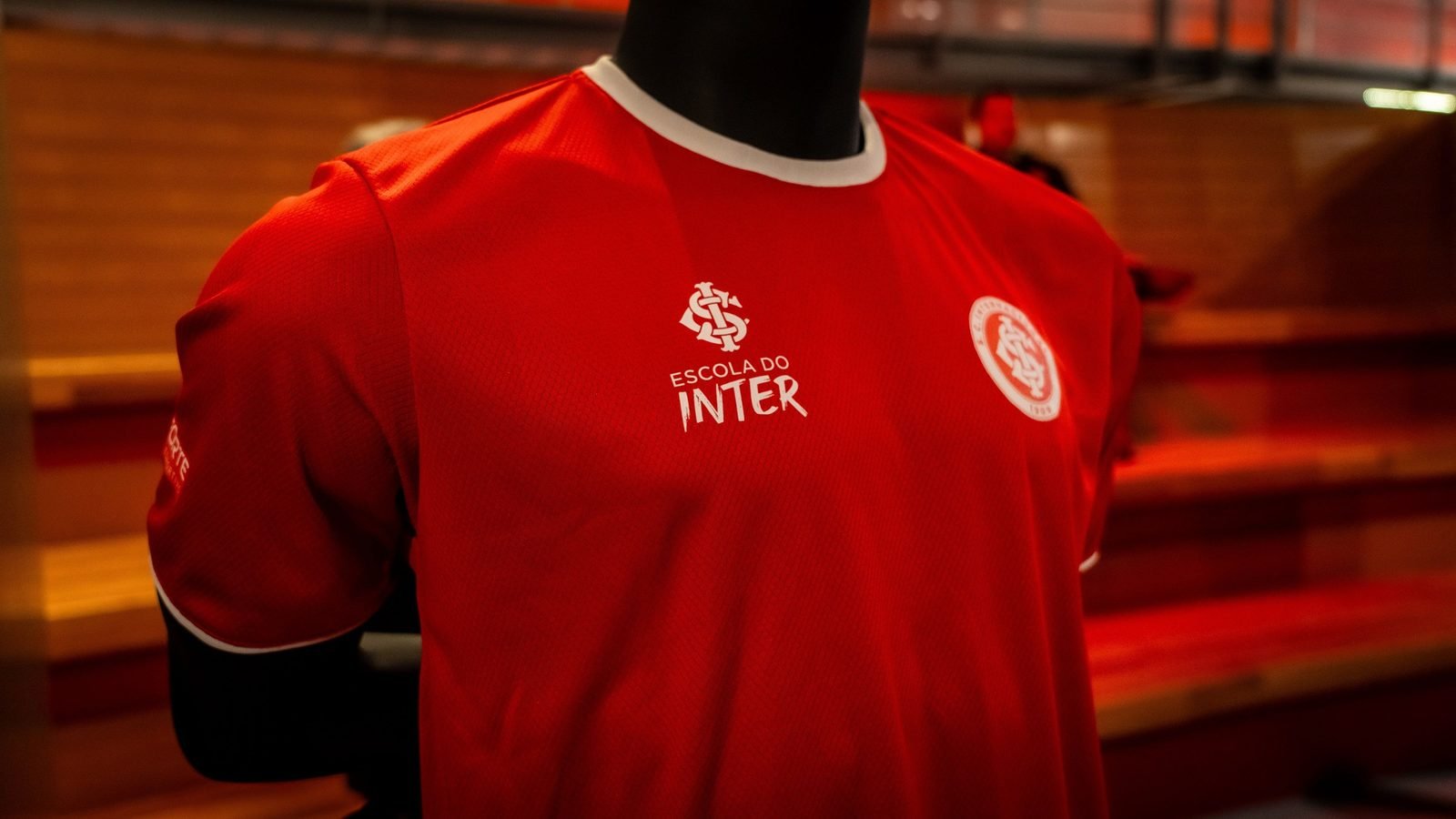 Camisa vermelha da Escola do Inter com o escudo do Internacional, exposta em manequim durante o evento de lançamento no Beira-Rio
