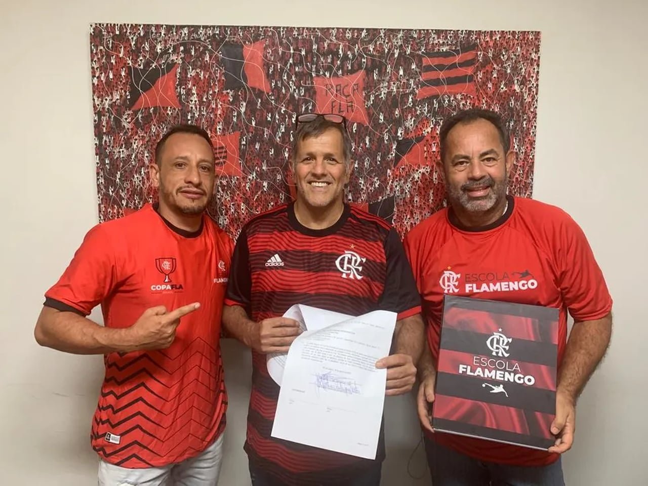 Três representantes com camisas do Flamengo exibem o contrato assinado e um quadro da Escola Flamengo