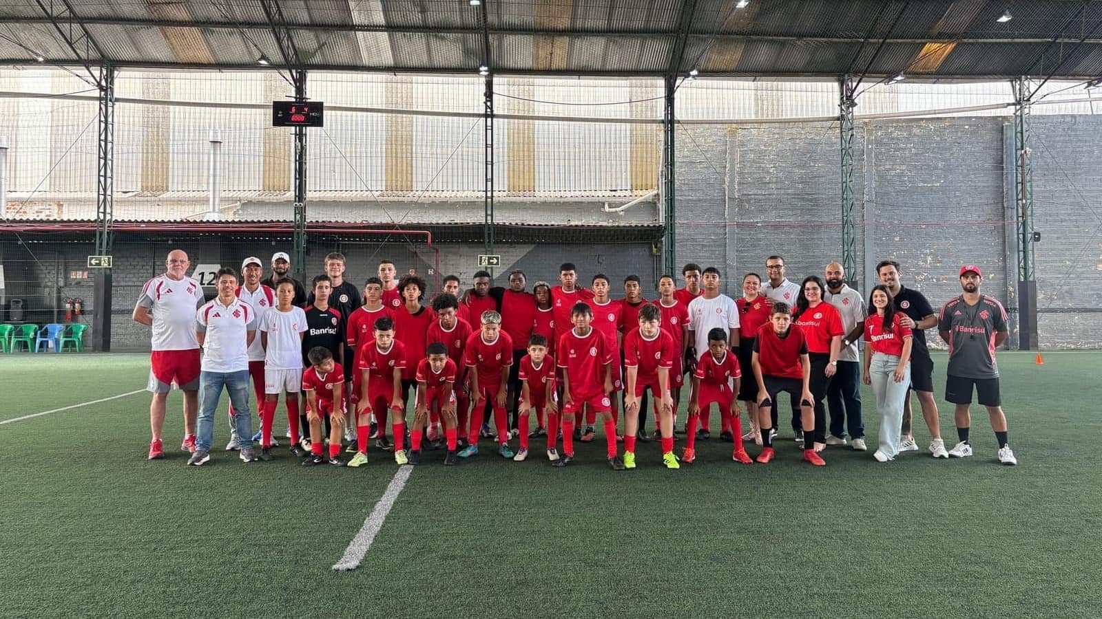 Students and coaches from an Escola do Inter unit gathered for a group photo at midfield, wearing Internacional's red kit