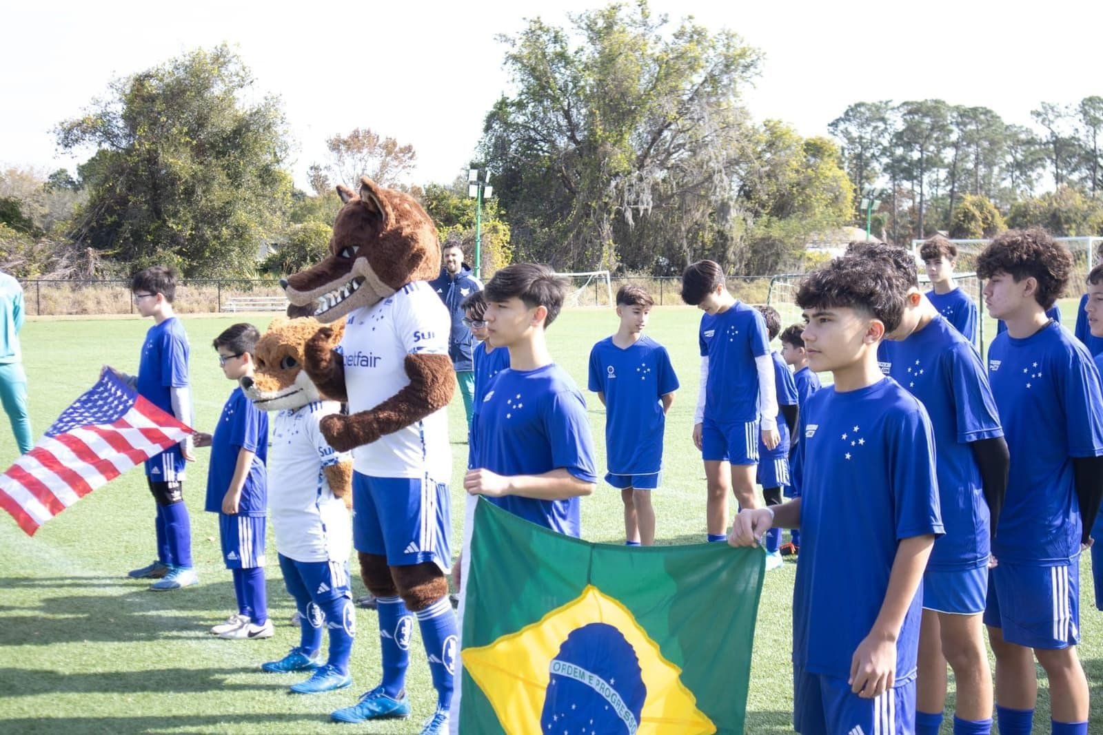 Atletas do Cruzeiro Camp perfilados com as bandeiras do Brasil e dos Estados Unidos ao lado do mascote do clube